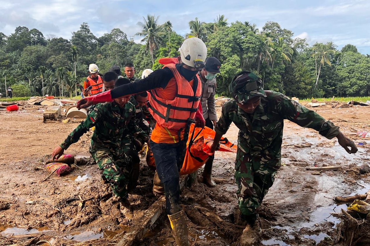 default-133 Rescue workers dressed in orange carry a body bag in muddy conditions.