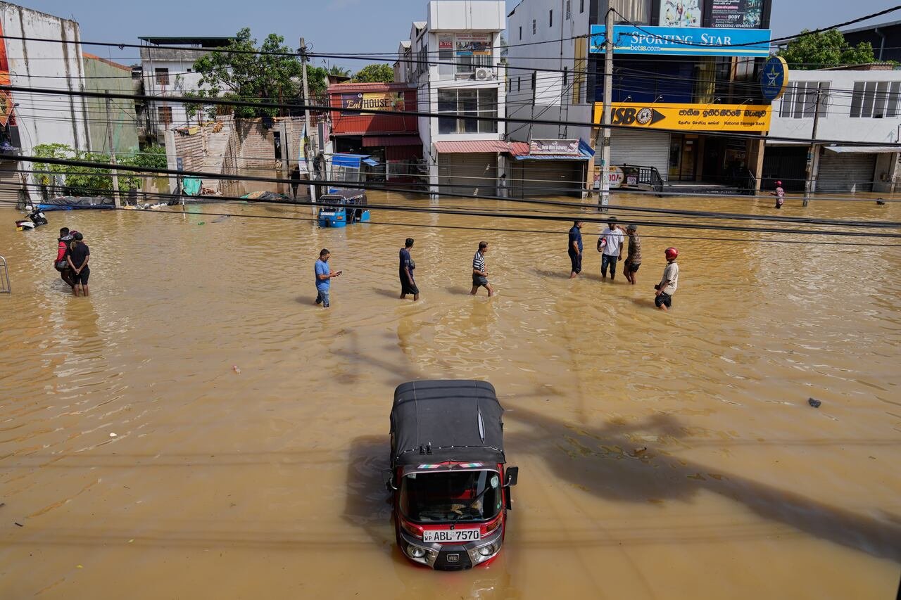 default-134 People walk through brown water as a truck is submerged on a sunny day in a city.