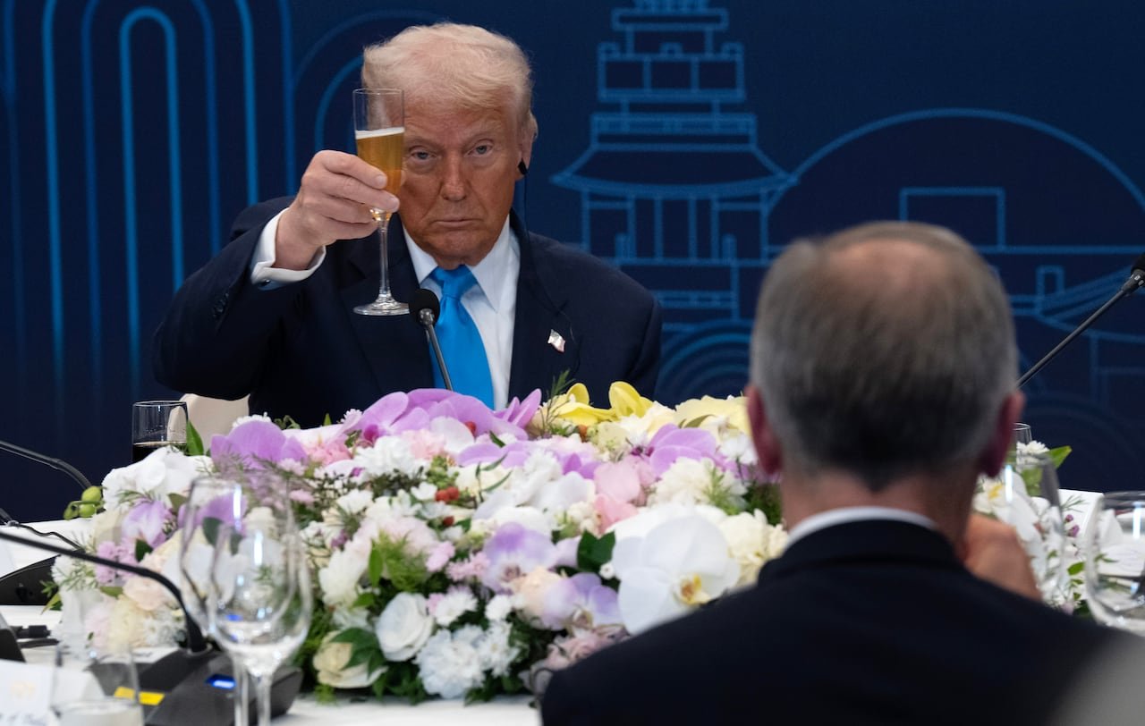 default-152 A man raises a glass of champagne, toasting another man seated across from him.