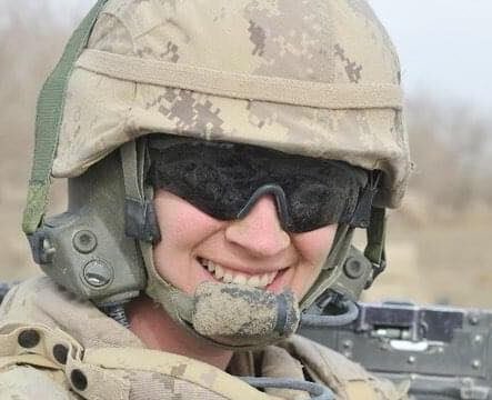 A woman wearing sunglasses and military gear is shown.