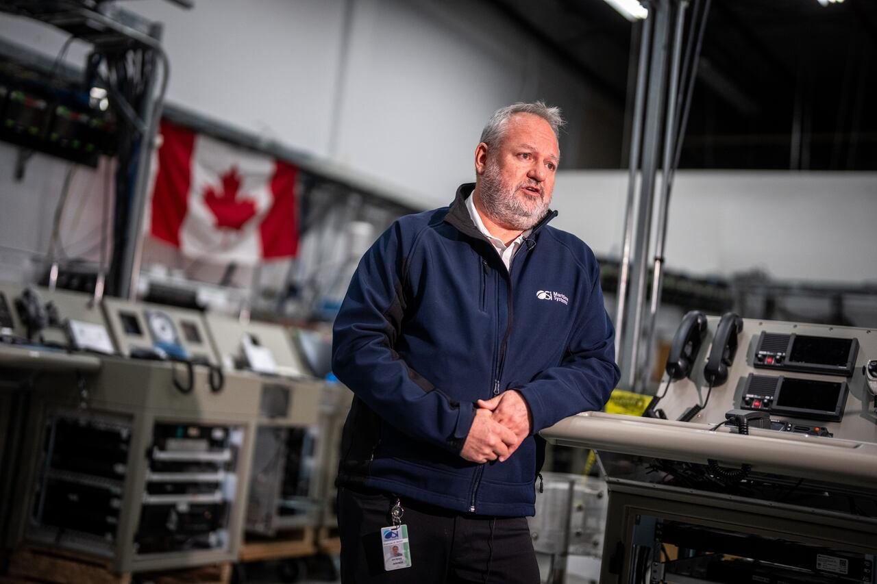 default-162 A man wearing a jacket stands inside a lab, with electronic consoles and a Canadian flag visible behind him.