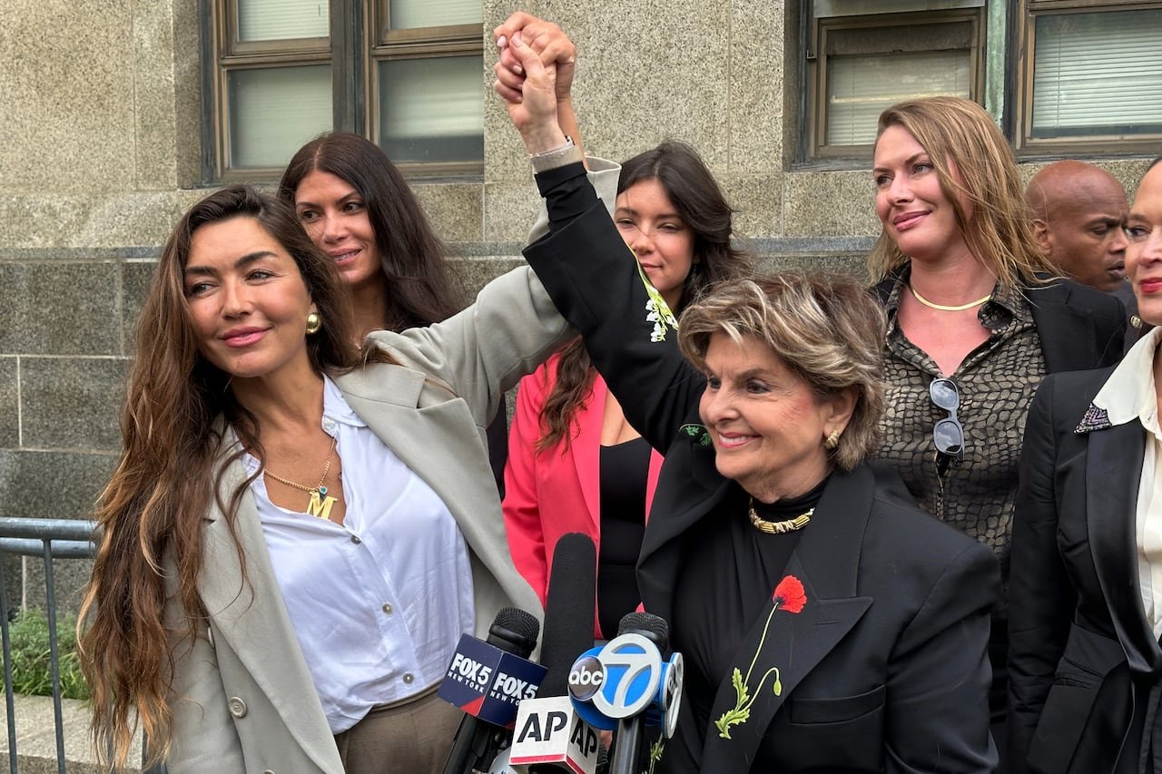 Two women triumphantly raise each other's arms in front of microphones while other women stand in the background.